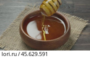 Drops of honey slowly flowing from a wooden honey dipper into a honey bowl, close-up. Honey flowing from a wooden honey dipper on to holland waffles. Стоковое видео, видеограф Андрис Салминьш / Фотобанк Лори