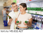 Friendly young couple selecting alcoholic beverages in supermarket. Стоковое фото, фотограф Яков Филимонов / Фотобанк Лори