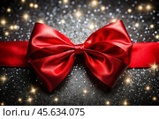 Elegant bow made of satin red ribbon on a shiny black background. Стоковое AI-изображение, AI-художник Photojuli / Фотобанк Лори
