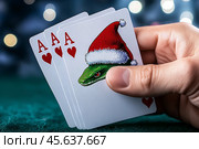 Карты в руке, тузы черви и джокер - зеленая змея в красной шапочке Санты. Удача в новом, 2025 году. Стоковое AI-изображение, AI-художник Щеголева Ольга / Фотобанк Лори