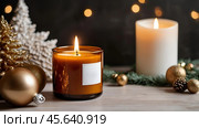 A mock-up of a cozy burning candle made of amber glass with an empty white label in a festive, New Year's home interior. Стоковое AI-изображение, AI-художник Photojuli / Фотобанк Лори