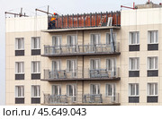 ANGARSK, IRKUTSK REGION, RUSSIA - October 08, 2024: Builders install light facade tiles on the top floor of a high-rise residential building. Urban residential construction concept. Редакционное фото, фотограф Виктория Катьянова / Фотобанк Лори