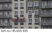 ANGARSK, IRKUTSK REGION, RUSSIA- October 08, 2024: Video of  builder descends in a suspended construction cradle after installing facade tiles on the wall of a high-rise modern residential building. Редакционное видео, видеограф Виктория Катьянова / Фотобанк Лори