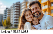 A happy family with a small child is smiling happily against the background of a new residential area. The concept of mortgages and housewarming. Стоковое AI-изображение, AI-художник Ярославский Максим / Фотобанк Лори