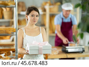 Cute young girl customer holding box with decorative bow and buying sweet authors flour products in bakery shop. Стоковое фото, фотограф Яков Филимонов / Фотобанк Лори