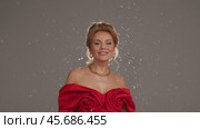 Artificial snow falls on the actress, wearing a red dress, in the studio while filming a music video. Slow motion. Стоковое видео, видеограф Strunov David / Фотобанк Лори