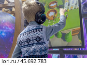 Immersion in world of technology: child wearing headphones interacts with an interactive screen. Стоковое фото, фотограф Алла Чесноковва / Фотобанк Лори