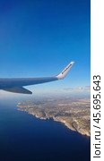 Ryanair airplane wing soaring over picturesque Maltese coastline cliff, showcasing deep blue sea and clear sky during flight: Luqa, Malta 9.01.2020. Редакционное фото, фотограф Kira_Yan / Фотобанк Лори
