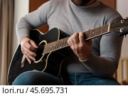 Playing the guitar. Strumming acoustic guitar. Musician plays music. Man fingers holding mediator. Man hand playing guitar neck in dark room. Unrecognizable person rehearsing, fretboard close-up. Стоковое фото, фотограф Марина Демидюк / Фотобанк Лори