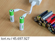 Two rechargeable batteries charged from power adapter, replacing many old batteries, environmental issues, Textured surface. Стоковое фото, фотограф Vladimir Vikhrov / Фотобанк Лори
