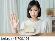 Young woman refusing slice of bread on plate with hand gesture. Стоковое AI-изображение, AI-художник Иван Рябоконь / Фотобанк Лори