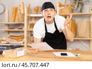 Bakery guy employee in apron examines documents, ponders debt restructuring. Стоковое фото, фотограф Яков Филимонов / Фотобанк Лори