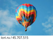 Colorful hot air balloon floating in blue sky with clouds. Стоковое AI-изображение, AI-художник Иван Рябоконь / Фотобанк Лори