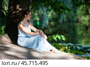 Beautiful young woman in a blue dress sits on the shore of a pond. Стоковое фото, фотограф Дмитрий Киселёв / Фотобанк Лори