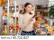 Girl customer holds bottle of peach juice in hand, scans QR code on product label. Стоковое фото, фотограф Яков Филимонов / Фотобанк Лори
