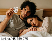 Пара лёжа в постели держит блистер презерватива. Стоковое AI-изображение, AI-художник Anna Leeva / Фотобанк Лори