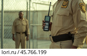 Prison guard holding walkie talkie monitoring inmate in penitentiary yard. Стоковое AI-изображение, AI-художник Юрий Поздников / Фотобанк Лори