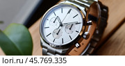 Luxury chronograph watch with white dial and steel bracelet resting on wooden surface. Стоковое AI-изображение, AI-художник Юрий Поздников / Фотобанк Лори