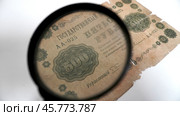 Антикварная банкнота 500 рублей 1918 года под лупой.  Фрагмент старинной купюры номиналом 500 рублей, датированной 1918 годом, рассматриваемой через увеличительное стекло. Видны детали оформления, включая орнаменты, номинал, серийный номер и текст о гарантиях обеспечения золотом. Банкнота имеет повреждения и следы износа, указывающие на её историческую ценность. Стоковое фото, фотограф Анна Чижова / Фотобанк Лори