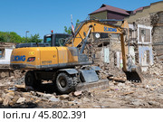 Колесный экскаватор XCMG XE210WD разбирает старые жилые дома солнечным майским днем. Дербент (2024 год). Редакционное фото, фотограф Виктор Карасев / Фотобанк Лори