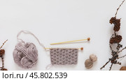 Video of winter knit and needlework. Knitting a warm scarf from soft beige wool yarn. Nearby are woolen balls and dry larch tree branches with cones on white background. Flat lay, top view, mock up. Стоковое видео, видеограф Виктория Катьянова / Фотобанк Лори