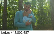 A bearded, joyful father in a baseball cap and blue jersey holds an infant dressed in a blue onesie. The father cradles his head against his son's head and kisses him tenderly. Family in nature. Стоковое видео, видеограф Воловодов Владимир / Фотобанк Лори