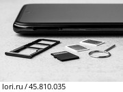 Smartphone with open slots for micro SD and nano SIM cards, two nano SIM cards and metal key on grey background black white photo. Стоковое фото, фотограф Андрей С / Фотобанк Лори
