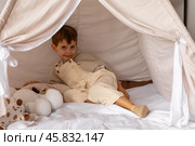Happy little caucasian boy is lying in a wigwam. Childhood, playing with soft toys, tenderness. Children's room with a teepee tent. Cozy atmosphere interior of a children's room. Стоковое фото, фотограф Ирина Михайличенко / Фотобанк Лори