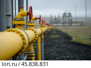 Gas Transportation With Gray Yellow Pipe Line and Valves On Outdoor Landscape Background with Large Industrial Plant. Oil Refinery And Pipeline. High pressure compressor station, energy infrastructure. Стоковое AI-изображение, AI-художник Марина Демидюк / Фотобанк Лори