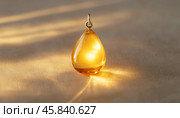 Teardrop shaped amber pendant shining on soft fabric in sunlight. Стоковое AI-изображение, AI-художник Юрий Поздников / Фотобанк Лори
