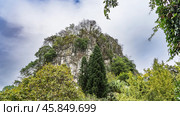 A picturesque mountain against the blue sky and clouds. There is green vegetation on the steep slopes and the top. Lush thickets of trees in the foreground. Fubo Hill. Guilin. China. Стоковое фото, фотограф Вера Ивановна Кубарева / Фотобанк Лори
