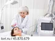 Elderly female beautician doing procedure of microneedling, mesotherapy for young woman in beauty salon indoors. Стоковое фото, фотограф Яков Филимонов / Фотобанк Лори