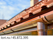 Close up of rain gutter on residential house roof with clay tiles on sunny day. Стоковое AI-изображение, AI-художник Иван Рябоконь / Фотобанк Лори