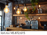 Hanging edison bulbs illuminating rustic coffee shop interior. Стоковое AI-изображение, AI-художник Иван Рябоконь / Фотобанк Лори
