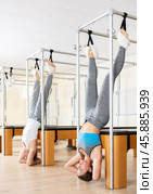Focused girl hanging upside down on trapeze table in Pilates studio. Стоковое фото, фотограф Яков Филимонов / Фотобанк Лори