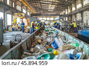 A recycling center, waste sorting facility bustling with activity. Workers sorting materials and machinery processing recyclables. Shallow depth of field. Стоковое AI-изображение, AI-художник Михаил Строгалев / Фотобанк Лори