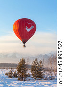 TUNKA VILLAGE, KYREN DISTRICT, BURYATIA, RUSSIA - January 04, 2025:  Tourists traveling on red hot air balloon over snowy peaks of Eastern Sayan Mountains during winter holidays. Редакционное фото, фотограф Виктория Катьянова / Фотобанк Лори