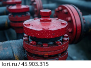A close-up of red industrial valves or gates that are part of a complex piping system. The red coloring likely serves to indicate a specific type of equipment (for example, handling hot or hazardous liquids). Drops of water are visible on the surface of the metal parts, which may indicate recent exposure to precipitation or a humid operating environment. The parts are connected with bolts, which ensures the tightness and stability of the structure. The black pipes create a contrast with the red elements, emphasizing their importance in the overall system.These elements are typical of industrial infrastructure associated with the transportation of water, oil, gas or other liquids. The photo conveys the atmosphere of the harsh working conditions inherent in industrial facilities. Стоковое AI-изображение, AI-художник Анна Кривицкая / Фотобанк Лори