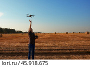 A man lands a quadcopter on his arm with a panoramic view of a mowed wheat field with straw bales. Стоковое фото, фотограф Роман Дзюбало / Фотобанк Лори
