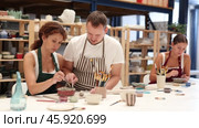 Experienced potter helps students learn how to make patterns on ceramic plates using paint and brush in a pottery workshop. Стоковое видео, видеограф Яков Филимонов / Фотобанк Лори