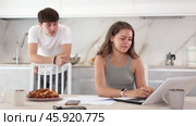 Sad young girl working on laptop while her boyfriend is quarreling with her standing behind in the kitchen. Стоковое видео, видеограф Яков Филимонов / Фотобанк Лори