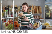 Smiling young girl with shopping basket trying to make choice holding two sorts of cheese in grocery store. Стоковое видео, видеограф Яков Филимонов / Фотобанк Лори