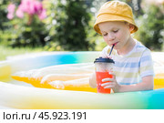 It's a hot summer day. Cute boy swims in the pool. The child drinks refreshing lemonade. The concept of summer holidays with children and refreshing drinks. Стоковое фото, фотограф Photojuli / Фотобанк Лори