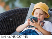 A 5-year-old little boy with a smartphone in his hands on the veranda. The child is playing on the phone. Harm of gadgets for children. Protect your child from the smartphone. Kids and gadgets. Стоковое фото, фотограф Photojuli / Фотобанк Лори