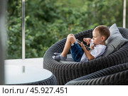 A 5-year-old little boy with a smartphone in his hands on the veranda. The child is playing on the phone. Harm of gadgets for children. Protect your child from the smartphone. Kids and gadgets. Стоковое фото, фотограф Photojuli / Фотобанк Лори