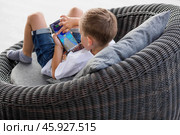 A 5-year-old little boy with a smartphone in his hands on the veranda. The child is playing on the phone. Harm of gadgets for children. Protect your child from the smartphone. Kids and gadgets. Стоковое фото, фотограф Photojuli / Фотобанк Лори
