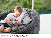 A 5-year-old little boy with a smartphone in his hands on the veranda. The child is playing on the phone. Harm of gadgets for children. Protect your child from the smartphone. Kids and gadgets. Стоковое фото, фотограф Photojuli / Фотобанк Лори