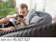 A 5-year-old little boy with a smartphone in his hands on the veranda. The child is playing on the phone. Harm of gadgets for children. Protect your child from the smartphone. Kids and gadgets. Стоковое фото, фотограф Photojuli / Фотобанк Лори