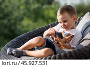 A 5-year-old little boy with a smartphone in his hands on the veranda. The child is playing on the phone. Harm of gadgets for children. Protect your child from the smartphone. Kids and gadgets. Стоковое фото, фотограф Photojuli / Фотобанк Лори