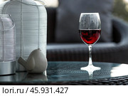 A glass of red alcoholic drink or wine on a glass table on the veranda. The concept of alcoholism, a party, or a holiday. Стоковое фото, фотограф Photojuli / Фотобанк Лори